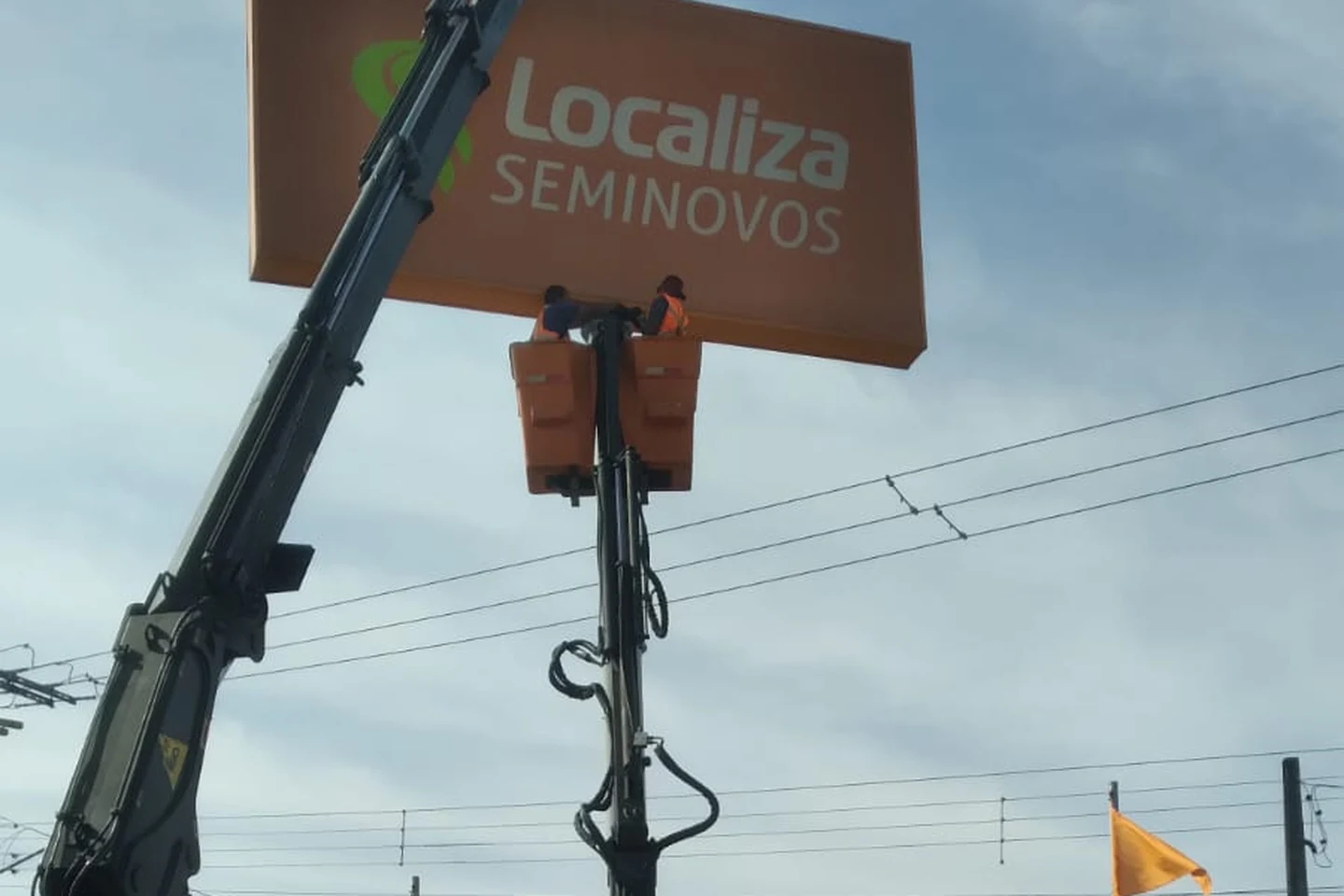 Cesto aéreo do munck da CLF com dois profissionais instalando um letreiro de concessionária